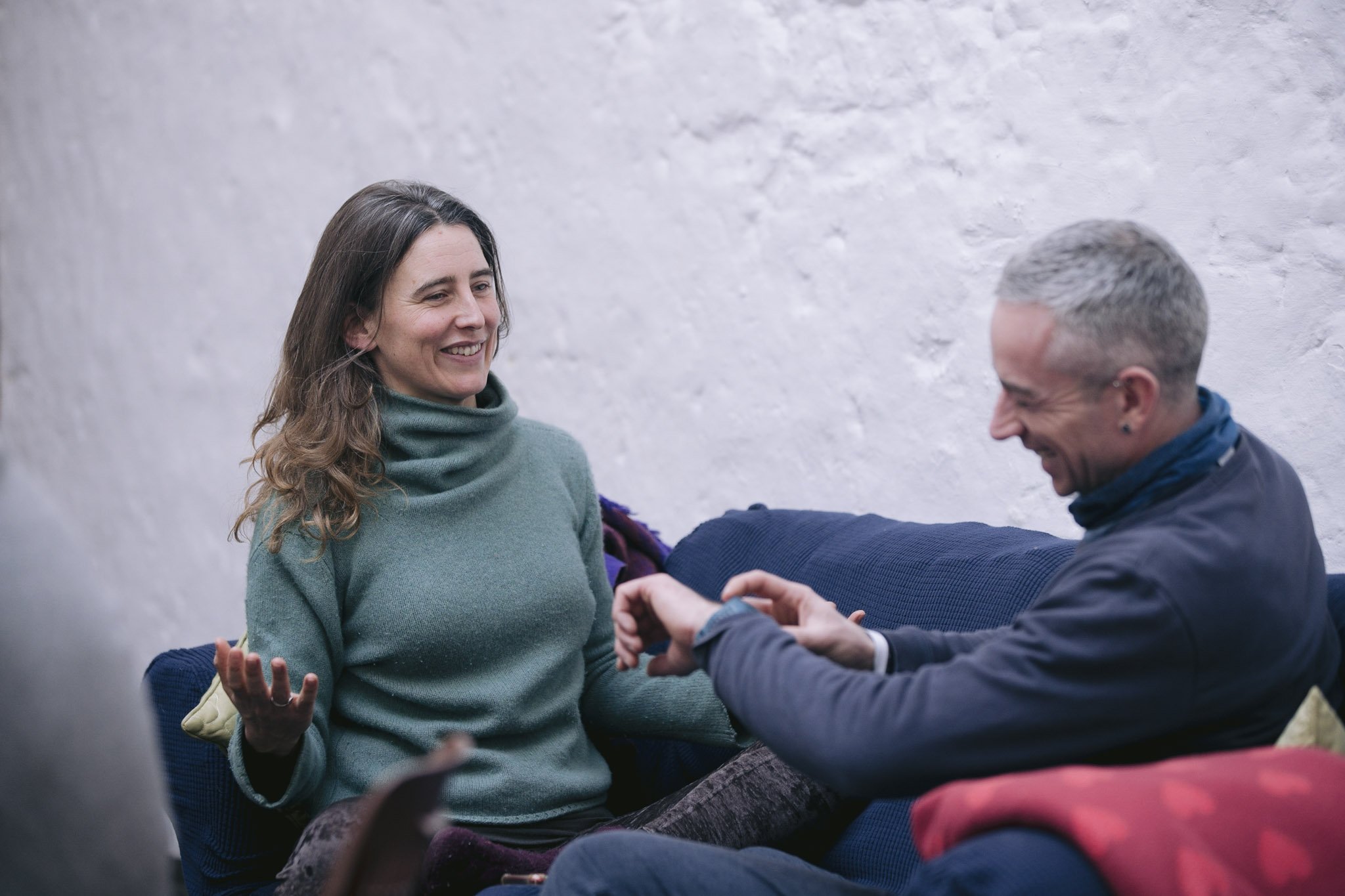 A woman and a man having a pleasant conversation on a sofa. The woman is smiling and gesturing with her hands while the man is laughing.