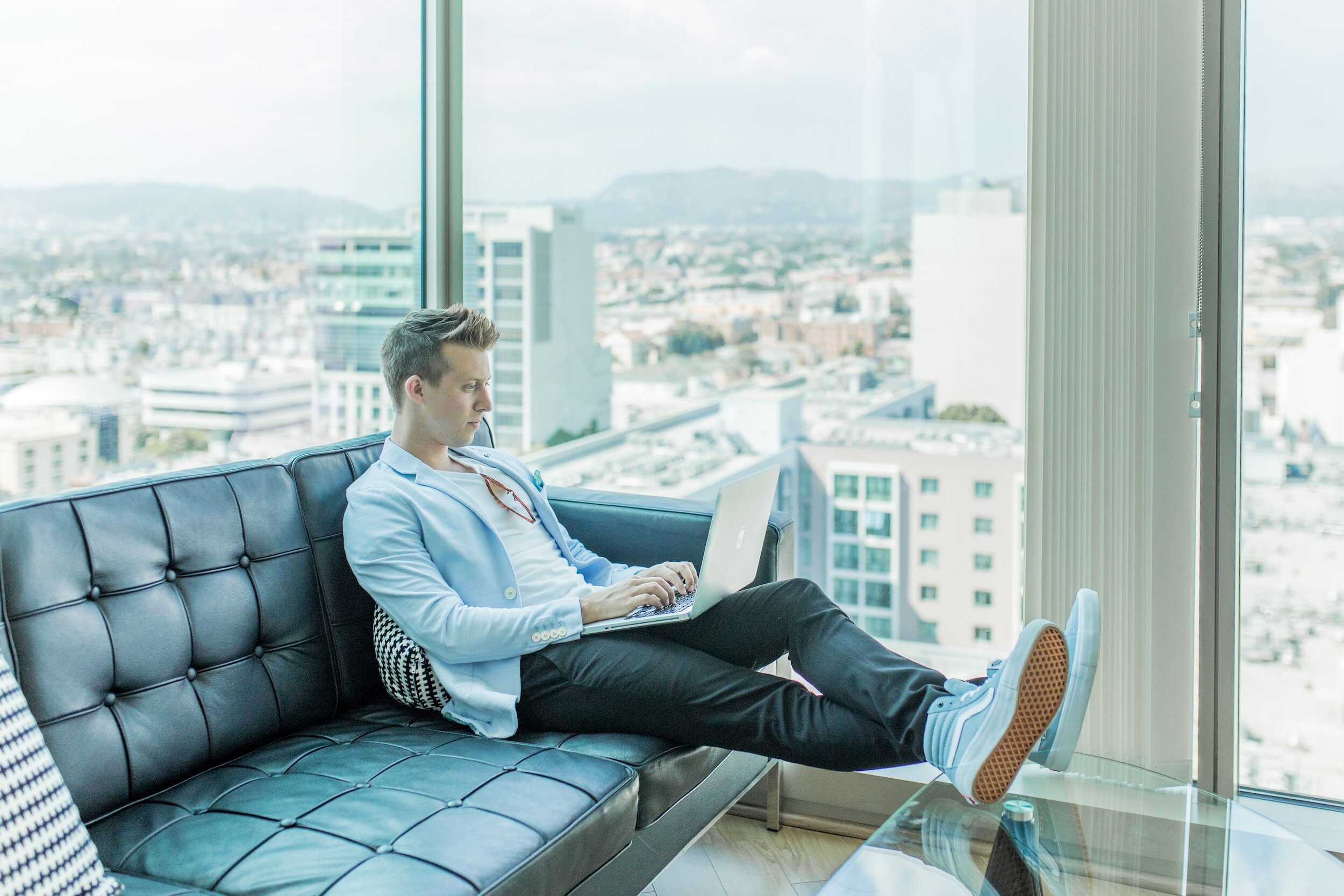 A man sitting on a couch working on his laptop with a view of the city in the background