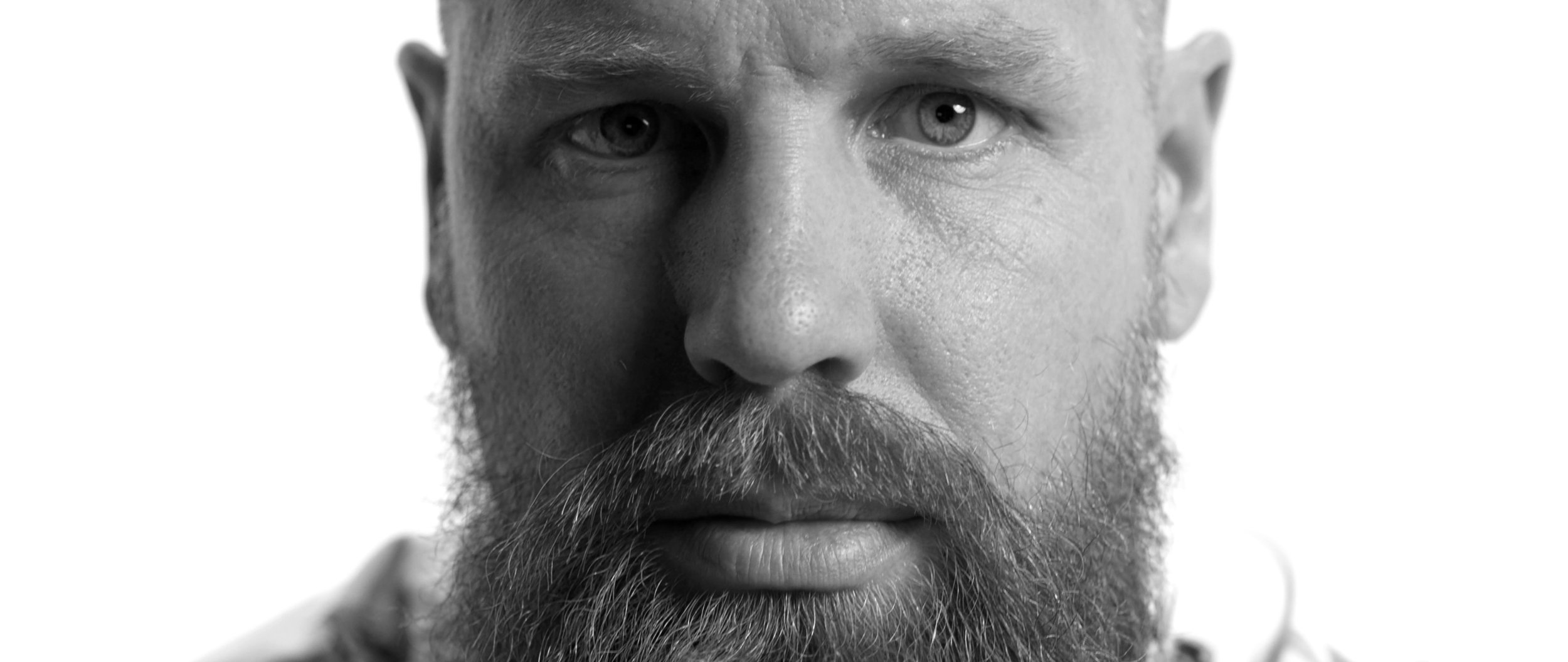 A close-up black and white portrait of a man with a thick beard and intense gaze, focusing on his expressive eyes.