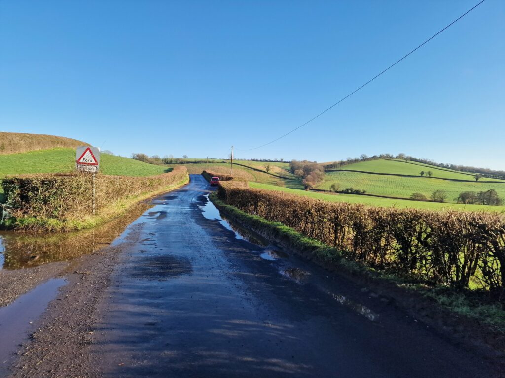 A scenic countryside road with green fields and a clear blue sky.