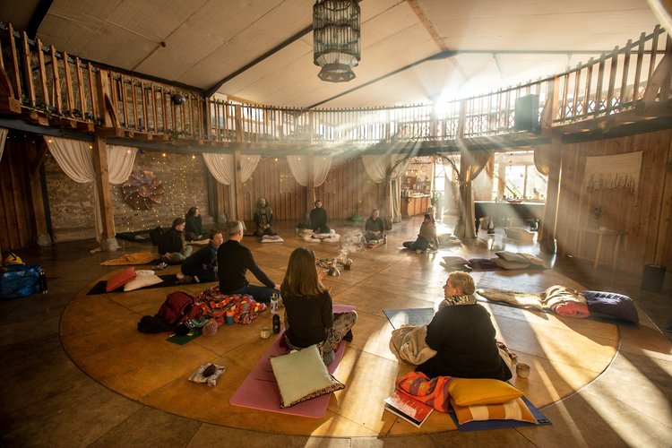 a room with people sitting on a circular carpet cross legged with the sun beaming through the window