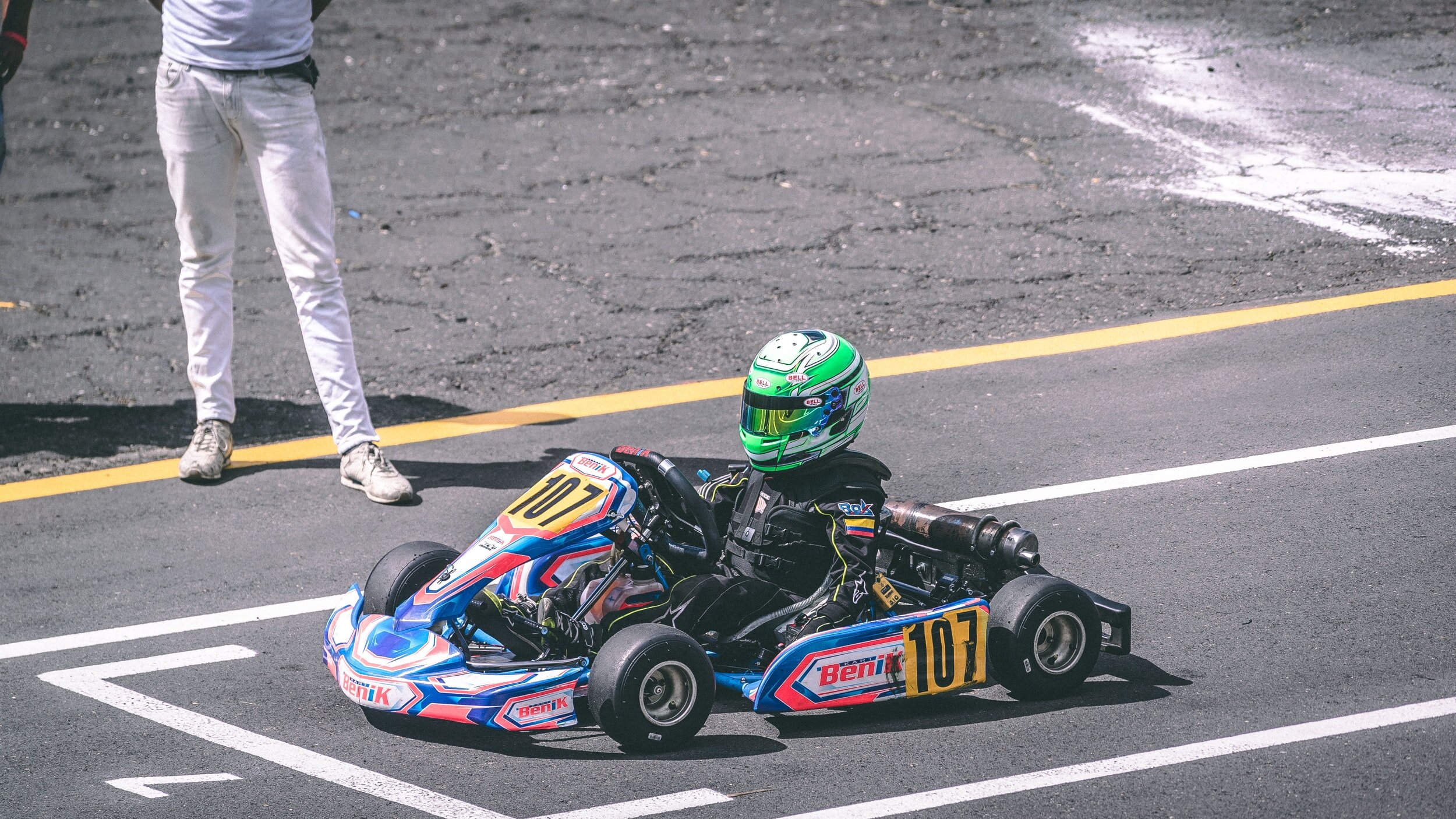 A go-kart racer in a blue and green kart on a race track.