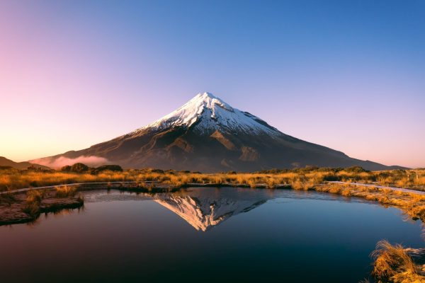 A stunning view of a snow-capped mountain reflected in a calm lake during sunrise.